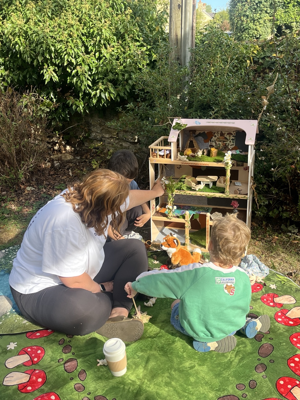 Children and a grown-up exploring a dolls’ house decorated with woodland animals and natural materials