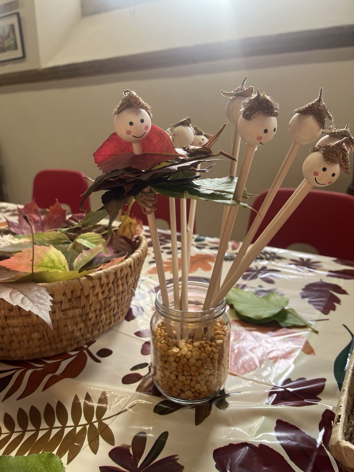 Handmade leaf people with wooden faces and seed-pod hats beside a basket of autumn leaves