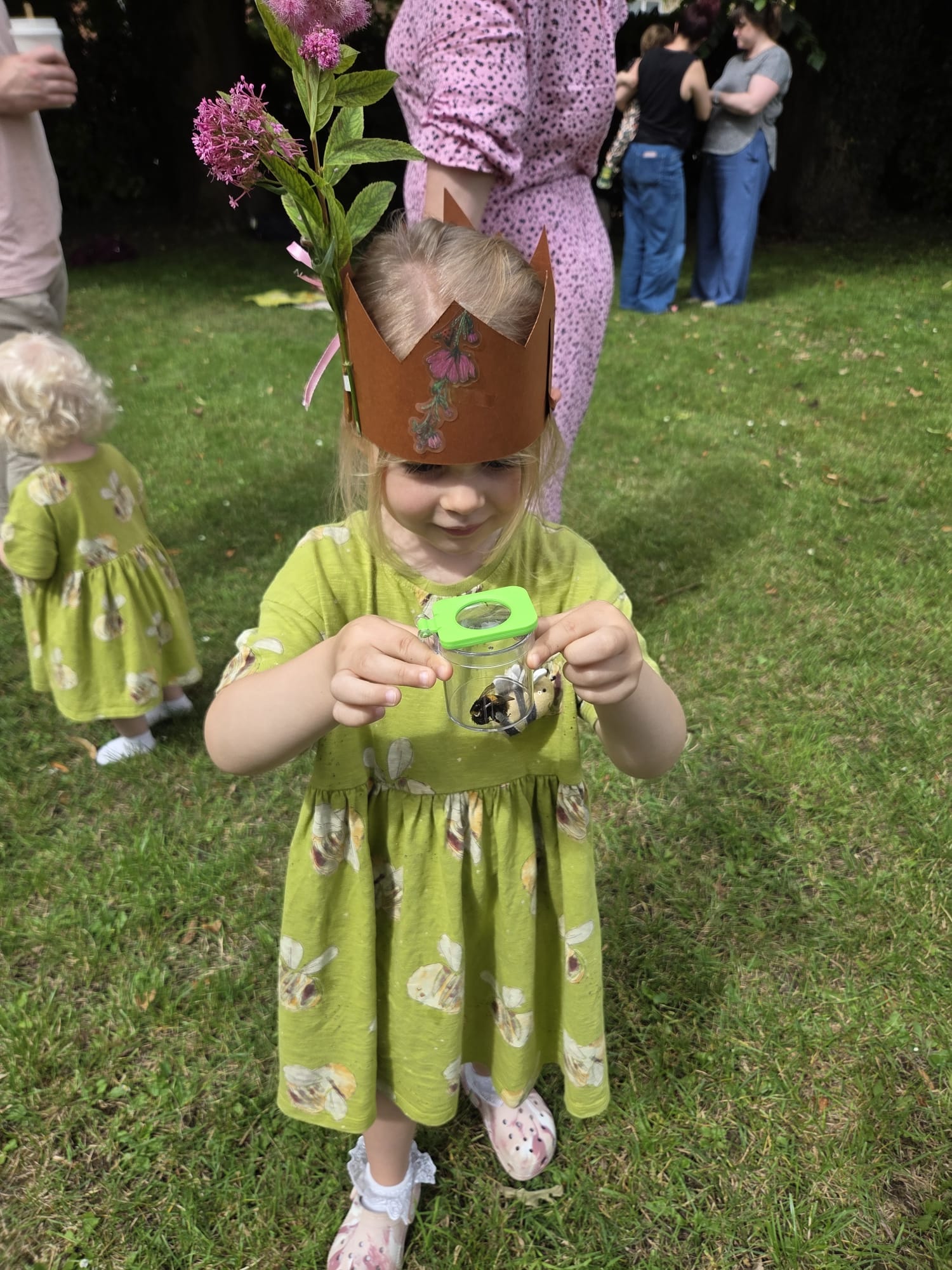 A child wearing a handmade nature crown and examining a small container