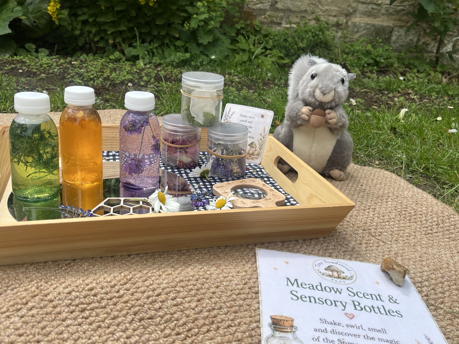 Colourful sensory bottles with flowers and a woodland puppet arranged on a wooden tray