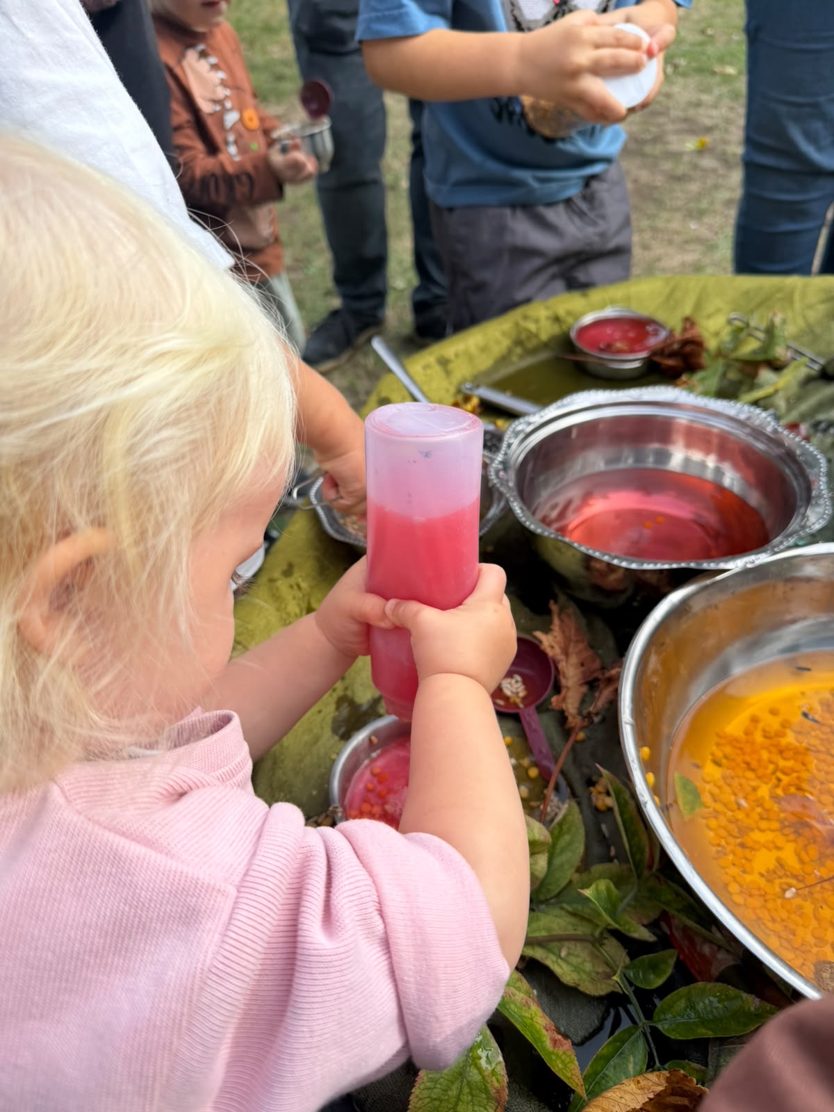 A child concentrating on pouring colourful liquid into a bowl at a potion invitation