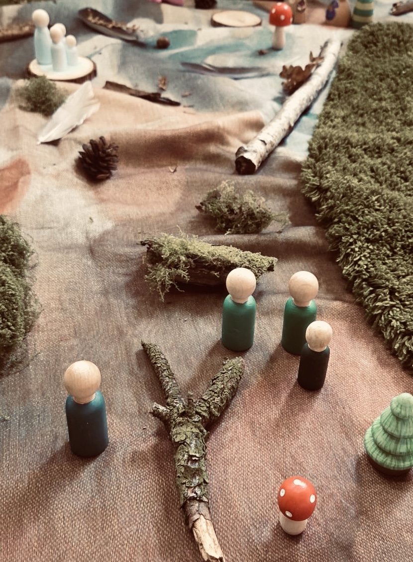 Peg people, pine cones, bark, moss and wooden toadstools arranged as a woodland small world